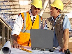 Two Men Wearing Hardhats in Discussion with Laptop Computer on Construction Site